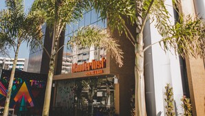 A modern building with a glass facade, a sign for 'Wonder House Hostel & Bar', and surrounding palm trees. - Wanderlust Hostel (Maceió)