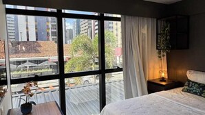 A modern hotel room with a large window, a bed, a desk, and a chair. - Wanderlust Hostel (Maceió)