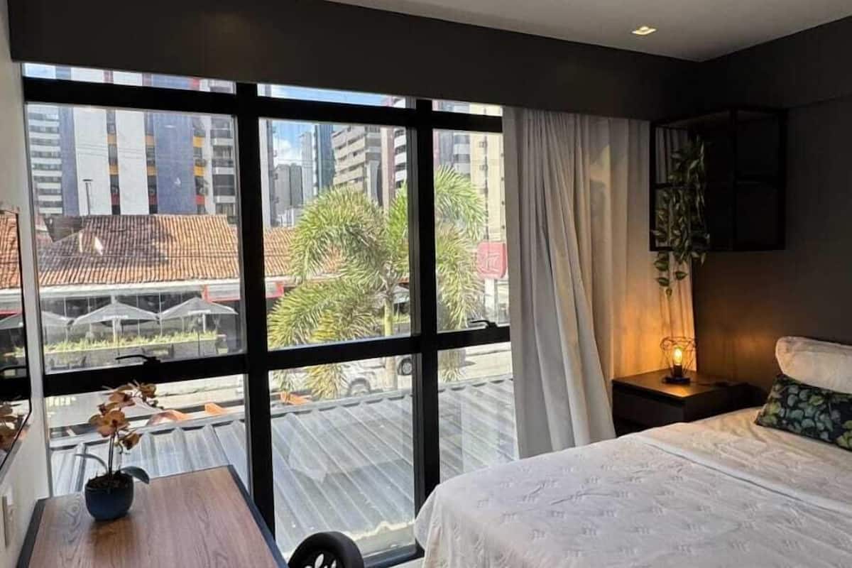 Quarto de hotel moderno com uma grande janela, uma cama, uma escrivaninha e uma cadeira.