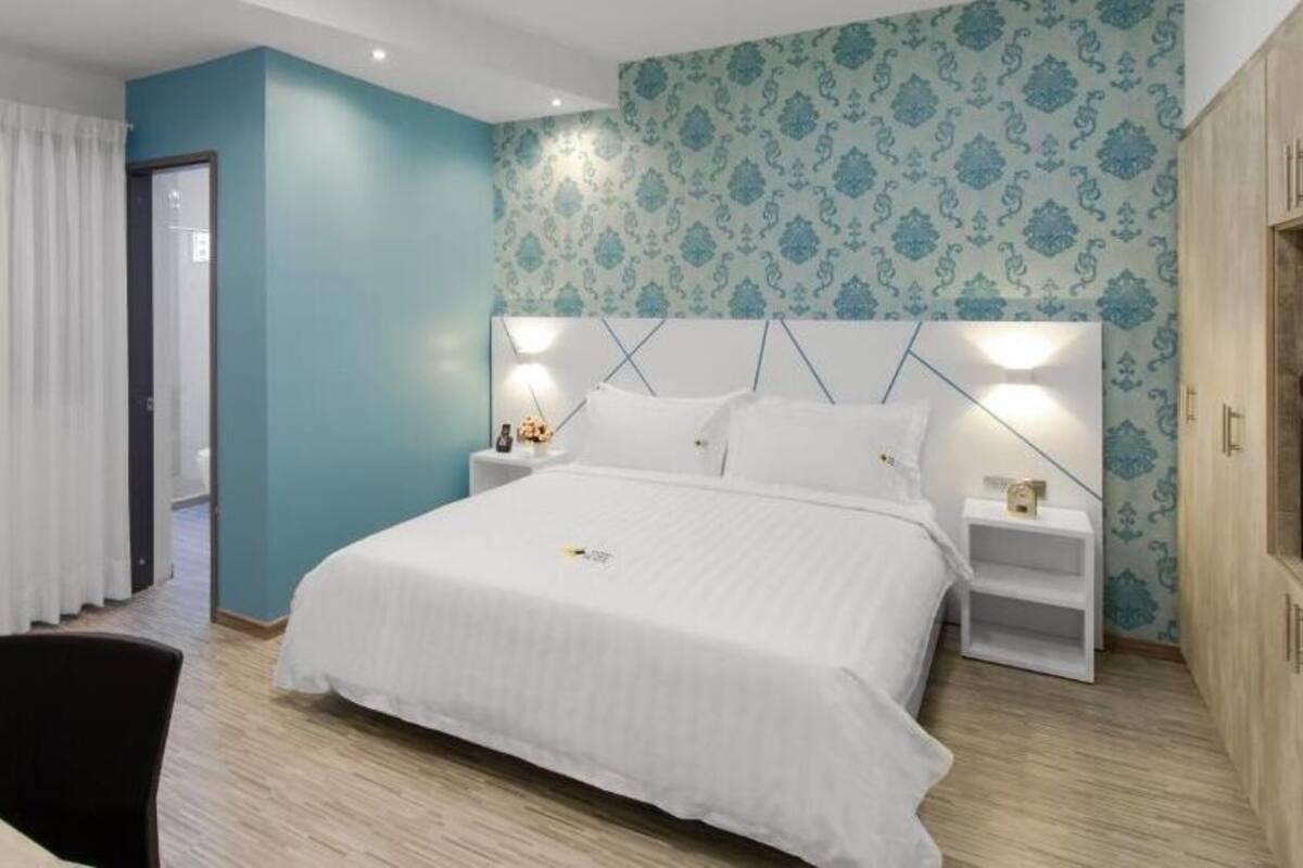 A modern hotel room with a large bed, a nightstand, a desk, and a wardrobe.