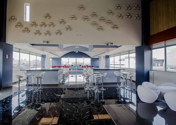 Zona de bar moderna con techos altos, vistas a la ciudad y un diseño de techo singular.