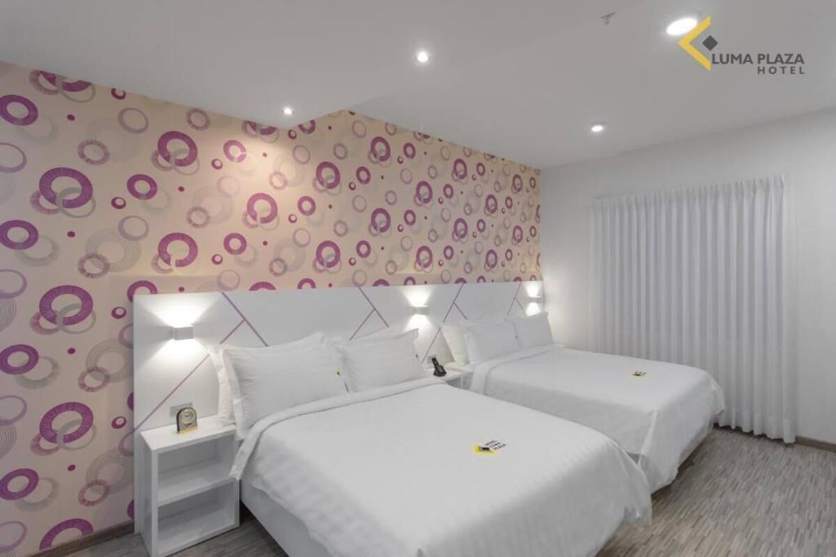 A hotel room with two beds, a patterned wall, and a window with curtains.