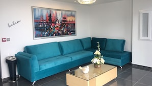 Un sofá color turquesa, una mesa de centro de vidrio con un adorno de pájaro, y una pintura de un paisaje urbano.