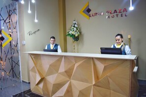 A reception desk at Luna Plaza Hotel with a geometric wood panel design, a reception sign, and a decorative plant. - Luma Plaza Hotel (Pereira)