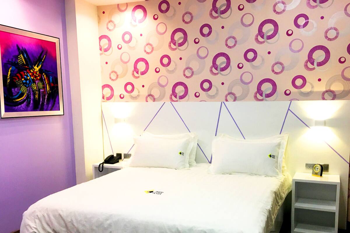 A modern hotel room with a large bed, two bedside tables, and a vibrant abstract painting on the wall.