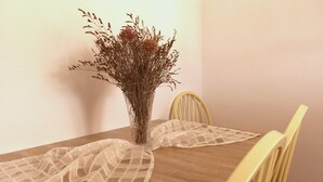 Ett matbord med en genomskinlig glasvas som innehåller torkade blommor, en spetsduk och en gul stol.