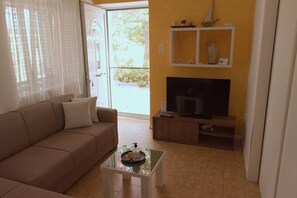 A living room with a sofa, a coffee table with a tray, a TV, and a shelf with decorative items.