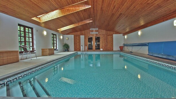 Una piscina al coperto con travi in legno a soffitto, acqua cristallina e bordi piastrellati.