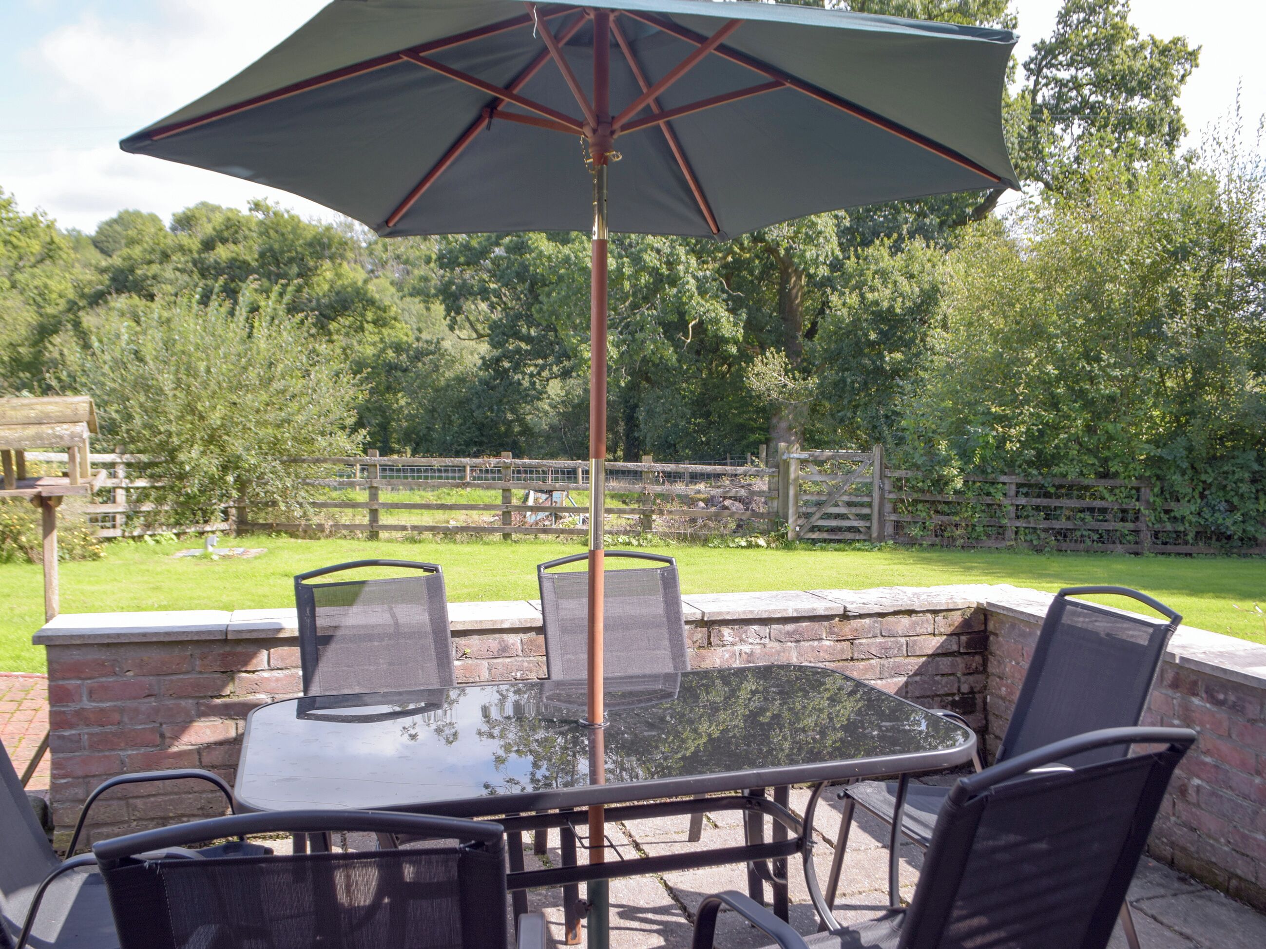 An outdoor patio with a glass table and chairs, a large umbrella, and a brick wall.