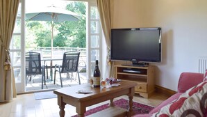 Un soggiorno con televisore, tavolino in legno e divano. C'è una zona pranzo e fuori dalla finestra un'area con sedie e un ombrellone.