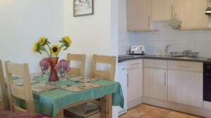 Un'area pranzo con tavolo apparecchiato per quattro persone, una cucina con mobili chiari e un singolo quadro appeso alla parete.