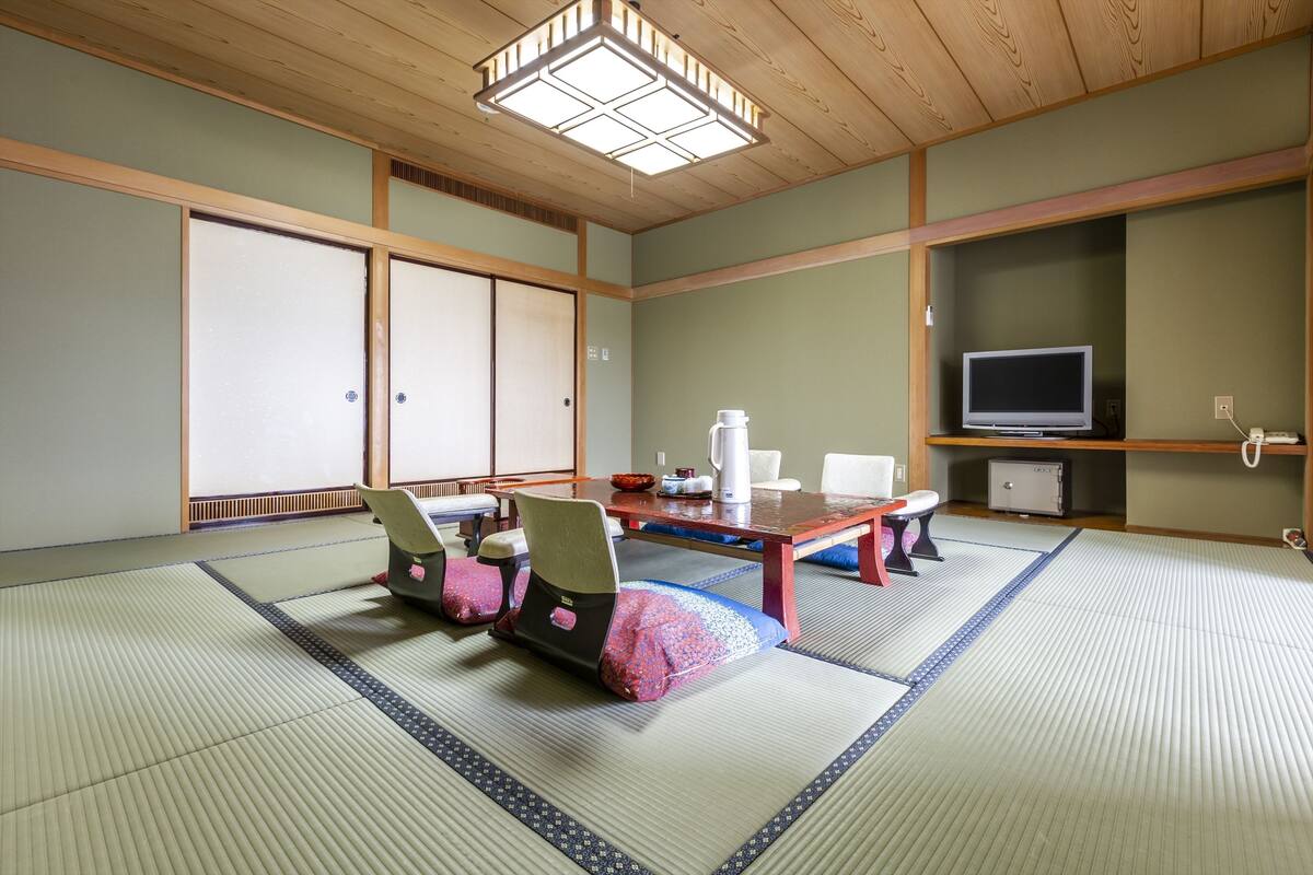 A tatami mat room with a low table, chairs, a television, and a cabinet.