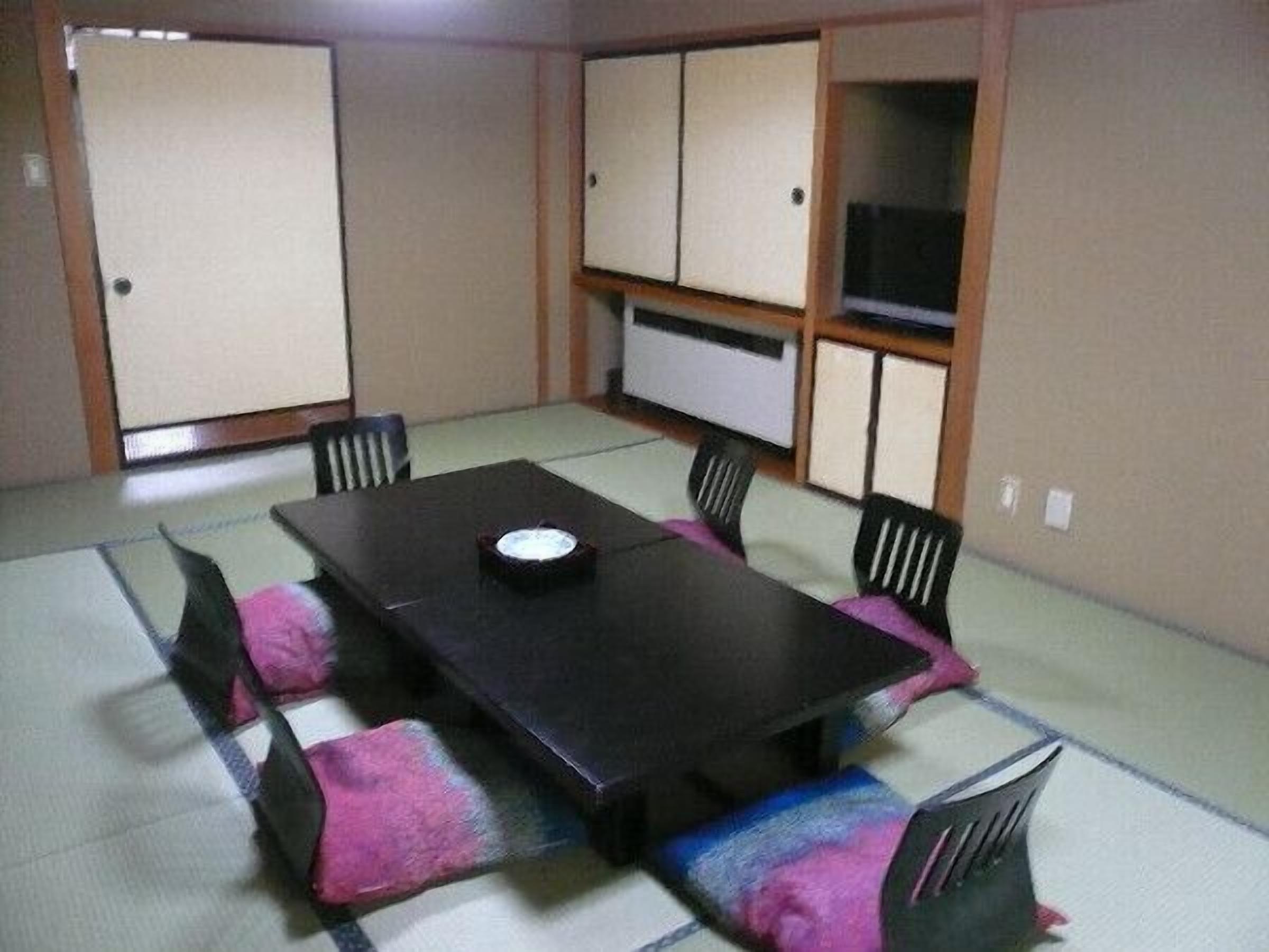 A tatami mat room with a low table and chairs, a television, and sliding doors.