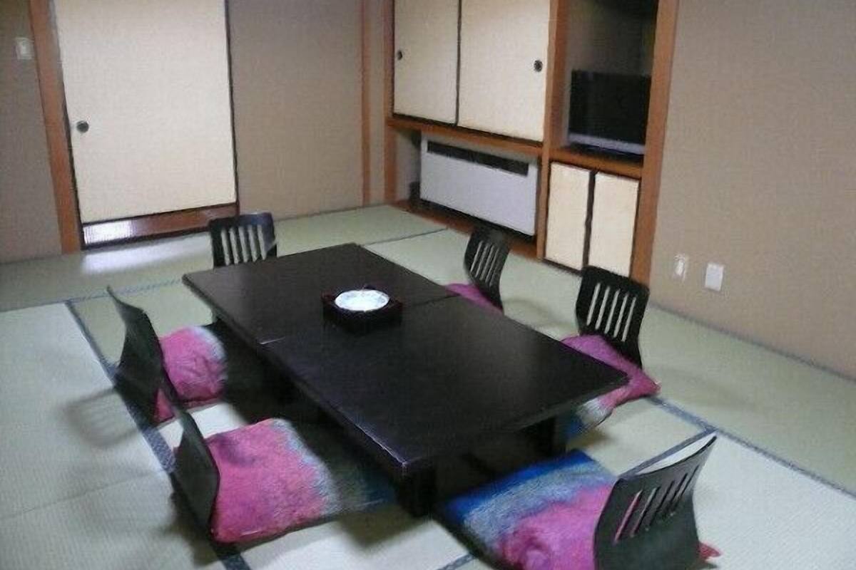 A tatami mat room with a low table and chairs, a television, and sliding doors.