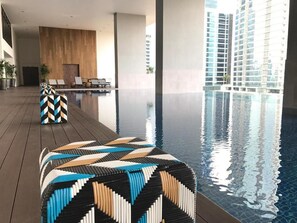 A modern indoor pool area with geometric-patterned seating and a view of tall buildings. - Cozy Family Suite Apartment (Kuala Lumpur)