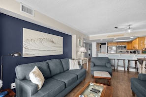 A living room with a sofa, armchairs, a coffee table, and a kitchen in the background.