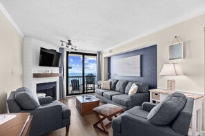 A living room with a fireplace, a television, a sofa, and a view of the outdoors.