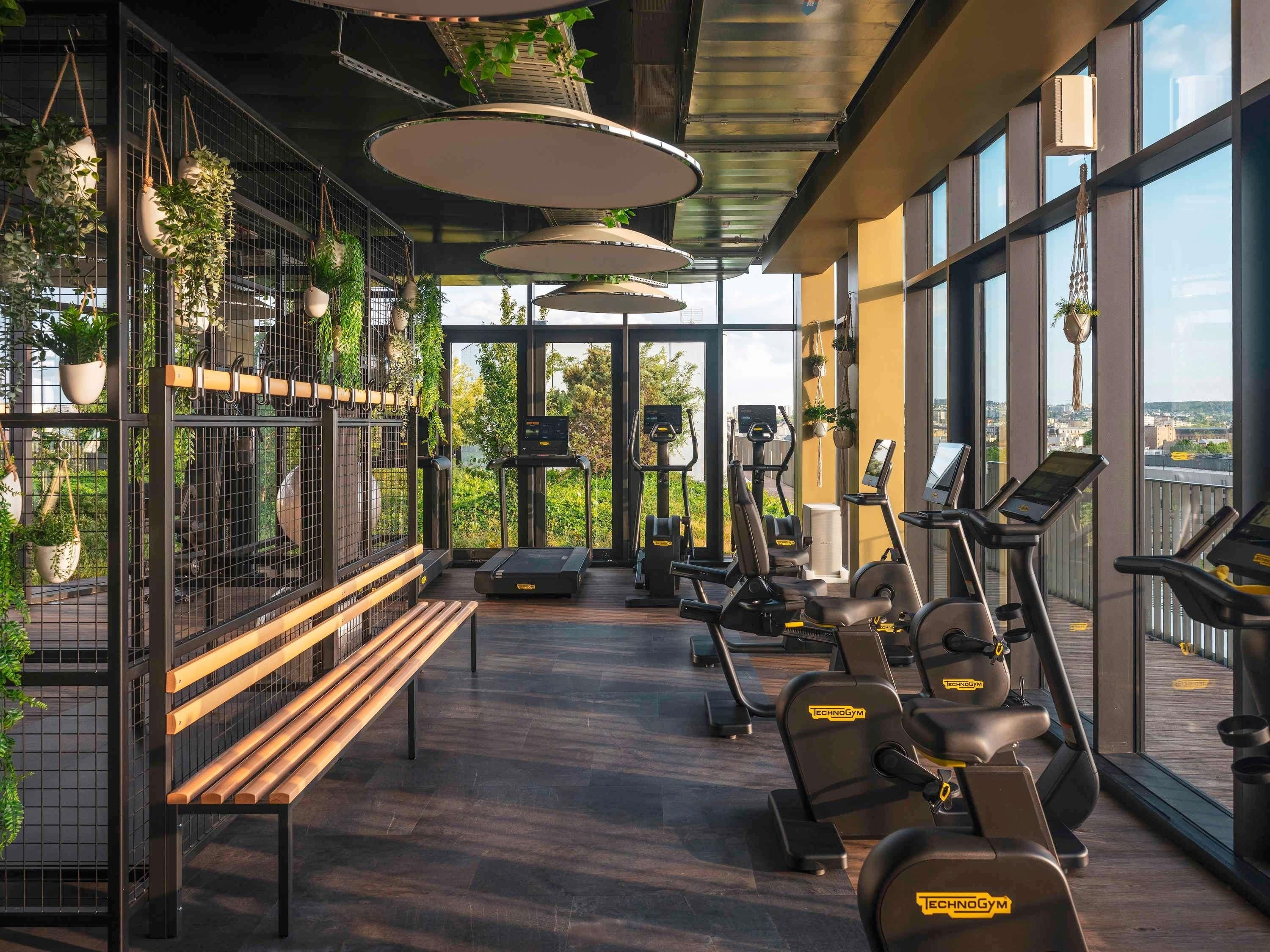 A gym with exercise equipment, a bench, and hanging plants.