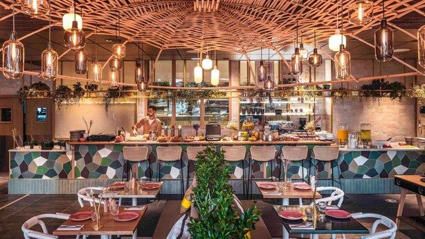 A restaurant with a high ceiling, hanging pendant lights, and a central bar area. - Novotel Paris Porte De Versailles (Paris)