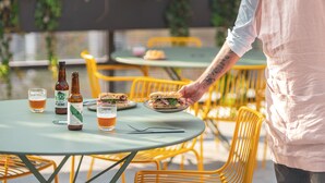 A person serving food at an outdoor table with chairs and a bottle of beer. - Novotel Paris Porte De Versailles (Paris)