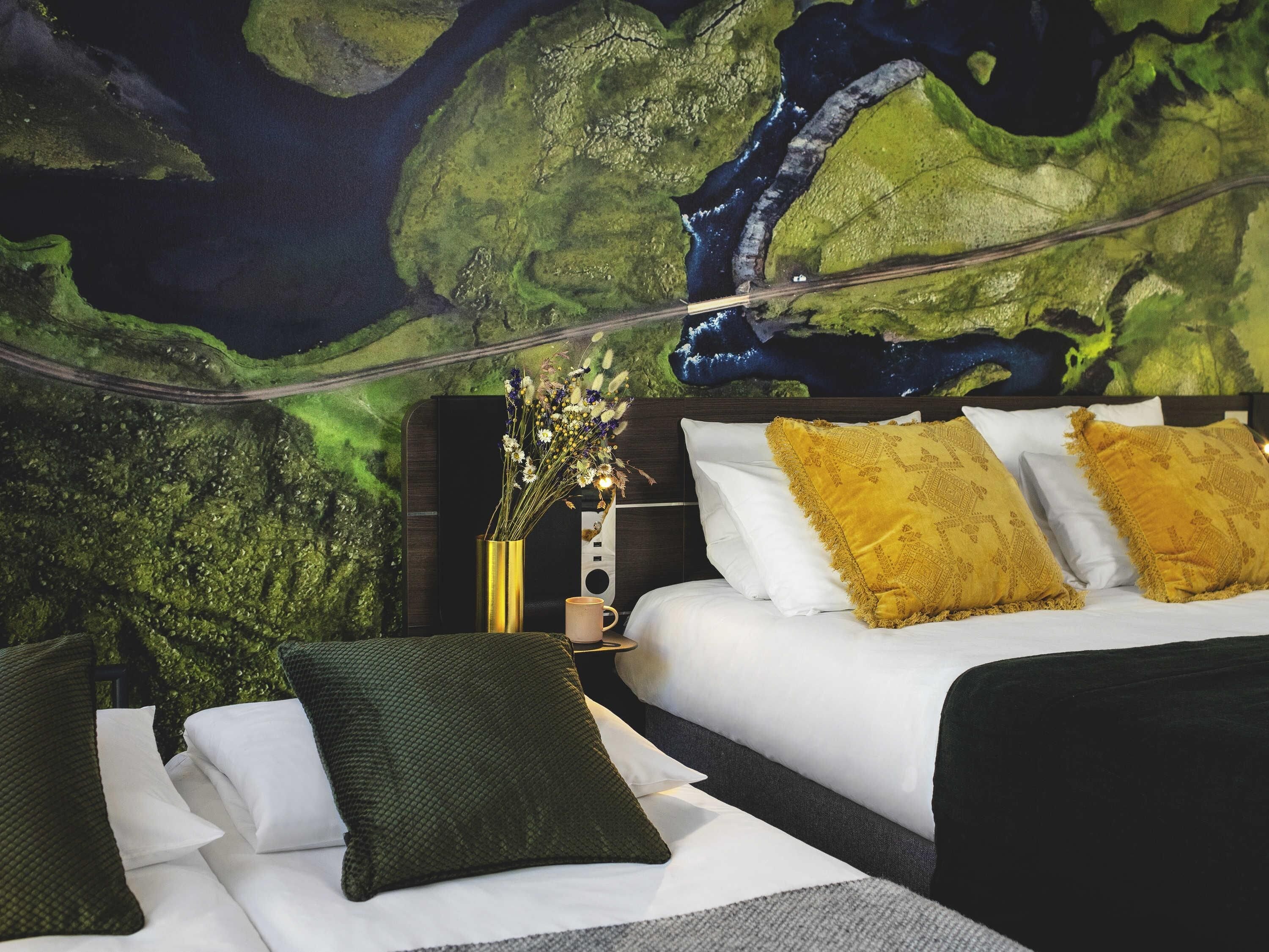 Una habitación con una cama, una mesita de noche y un mural en la pared que representa un paisaje.