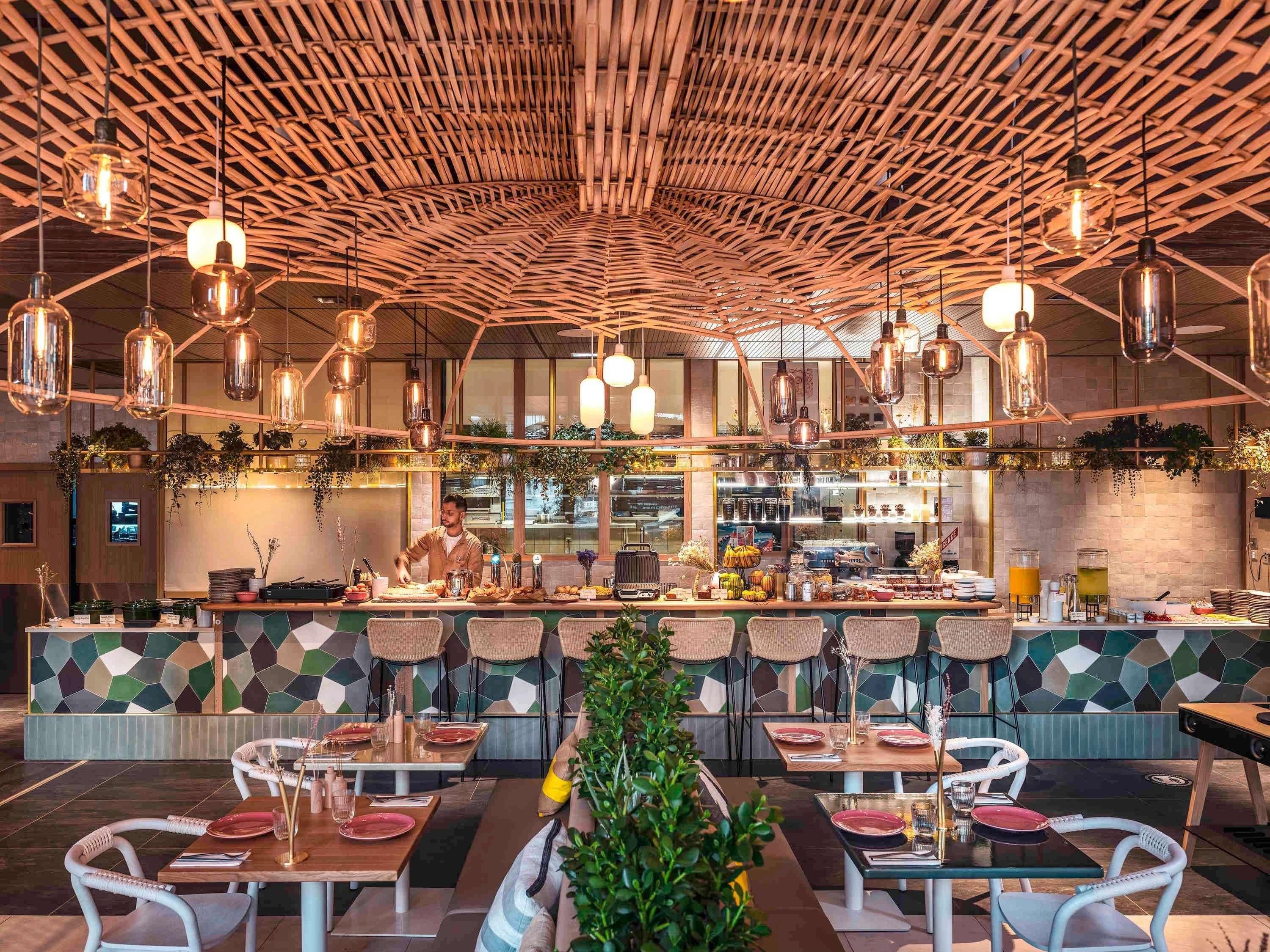 A restaurant with a high ceiling, hanging pendant lights, and a central bar area.