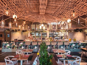 A restaurant with a high ceiling, hanging pendant lights, and a central bar area. - Novotel Paris Porte De Versailles (Paris)