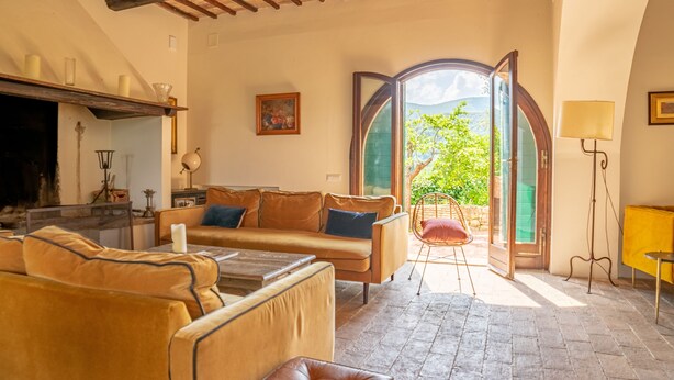 A cozy living room with a sofa, a coffee table, and a fireplace. There is a door leading to an outdoor area with a view of greenery. - Delightful secluded Tuscan farmhouse with pool, near the hilltop town of Cetona. (Cetona, SI)
