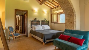 A bedroom with a bed, a chair, a sofa, and a stone wall. - Delightful secluded Tuscan farmhouse with pool, near the hilltop town of Cetona. (Cetona, SI)