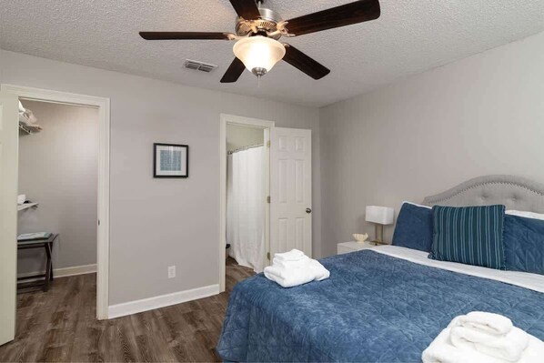A bedroom with a bed, a ceiling fan, a nightstand, and a door leading to another room.