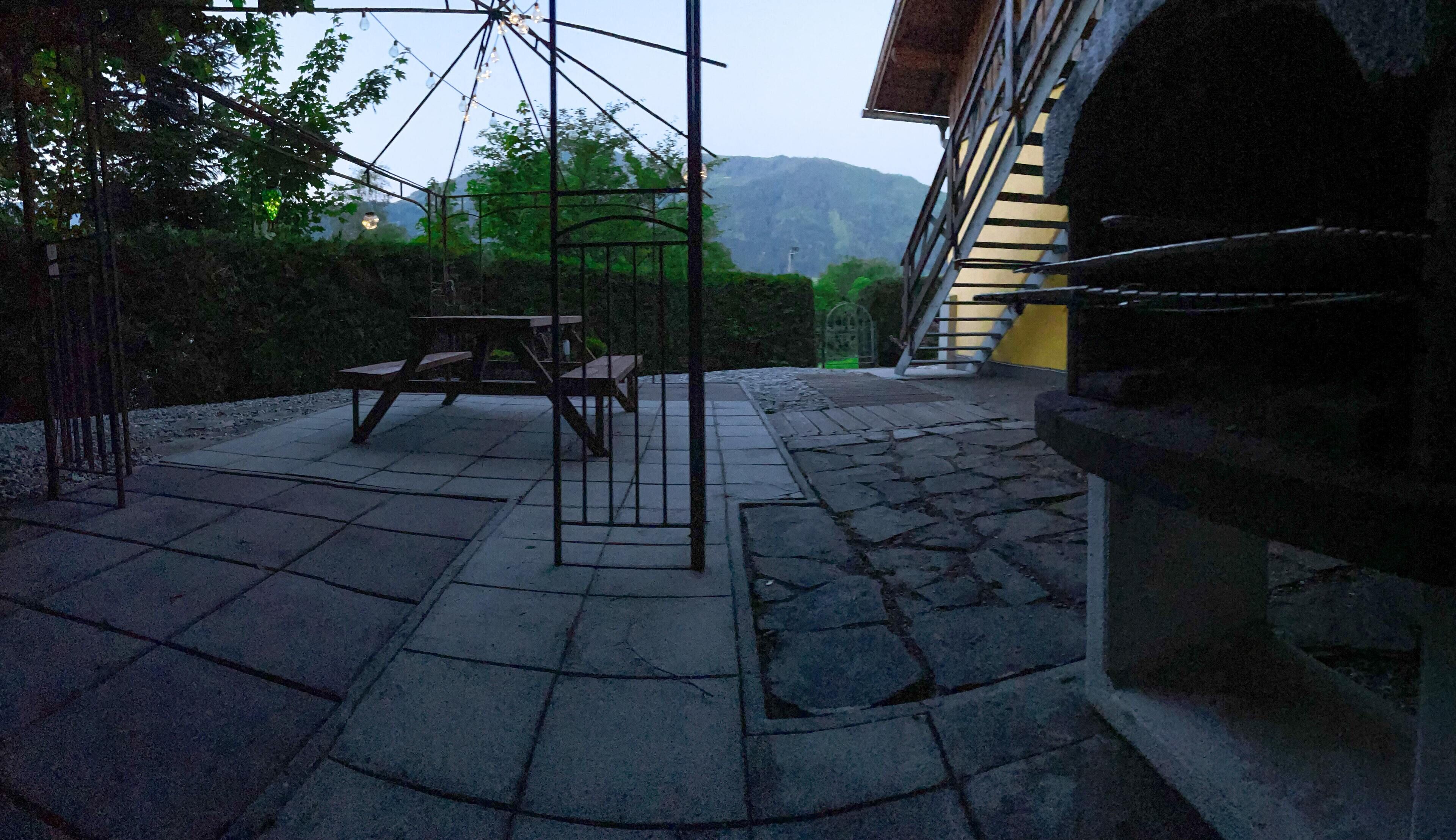 Un patio con suelo de piedra, una pérgola de metal y una mesa y banco de madera.