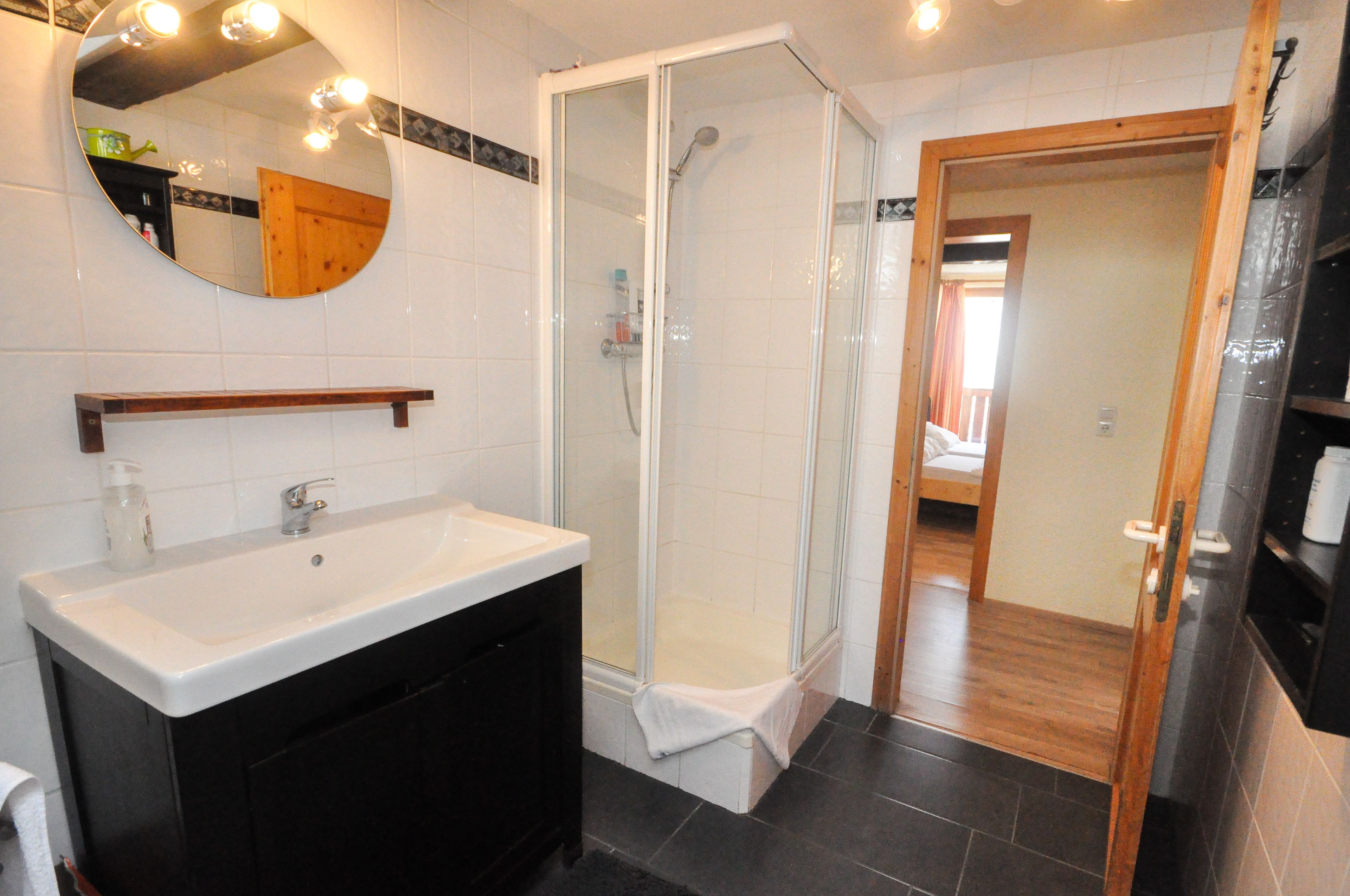 Un bagno moderno con un lavandino bianco, una cabina doccia in vetro e una porta in legno che dà su un'altra stanza.