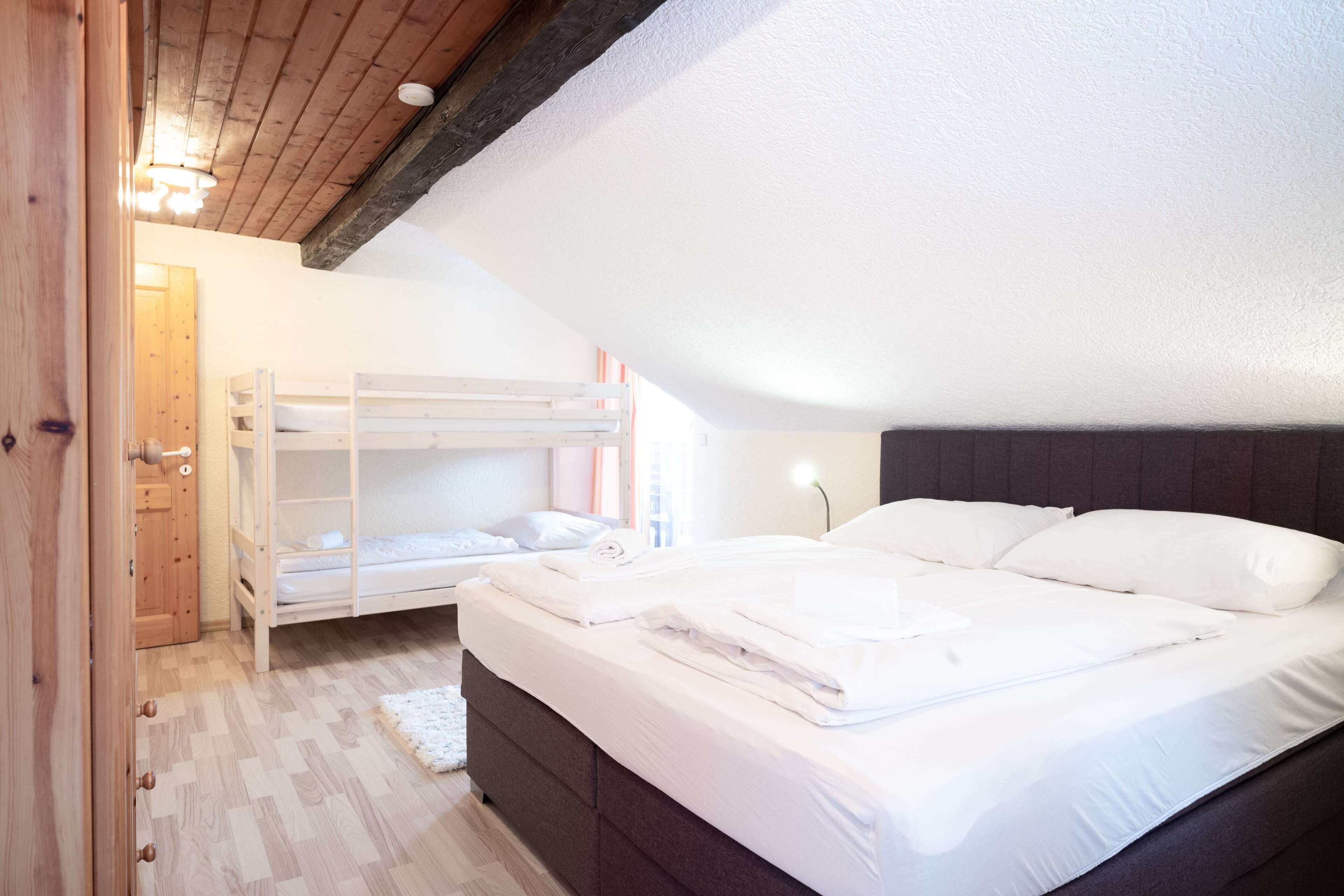 Camera da letto con un letto a castello, un letto singolo, pavimento in legno e soffitto bianco.