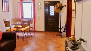 Un soggiorno con tavolo da pranzo in vetro, sedie in vimini, un divano in pelle scura, una TV a parete e una porta con finestra.