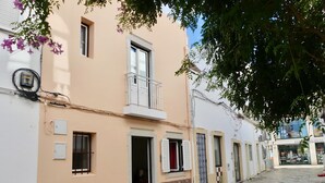Una strada con un edificio con un balcone, un negozio con un'insegna e un pavimento in pietra.