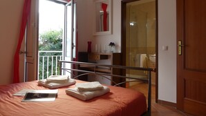 Una camera da letto con un letto, una finestra con tende rosse, un bagno con porta in vetro e una porta in legno.