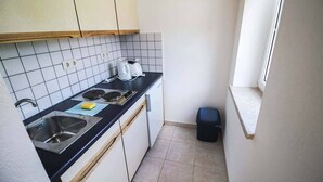 A compact kitchen with white cabinets, a black countertop, a sink, and a window. - Haus Sonnenwalde - Familie Ruhe (Rohrbach)