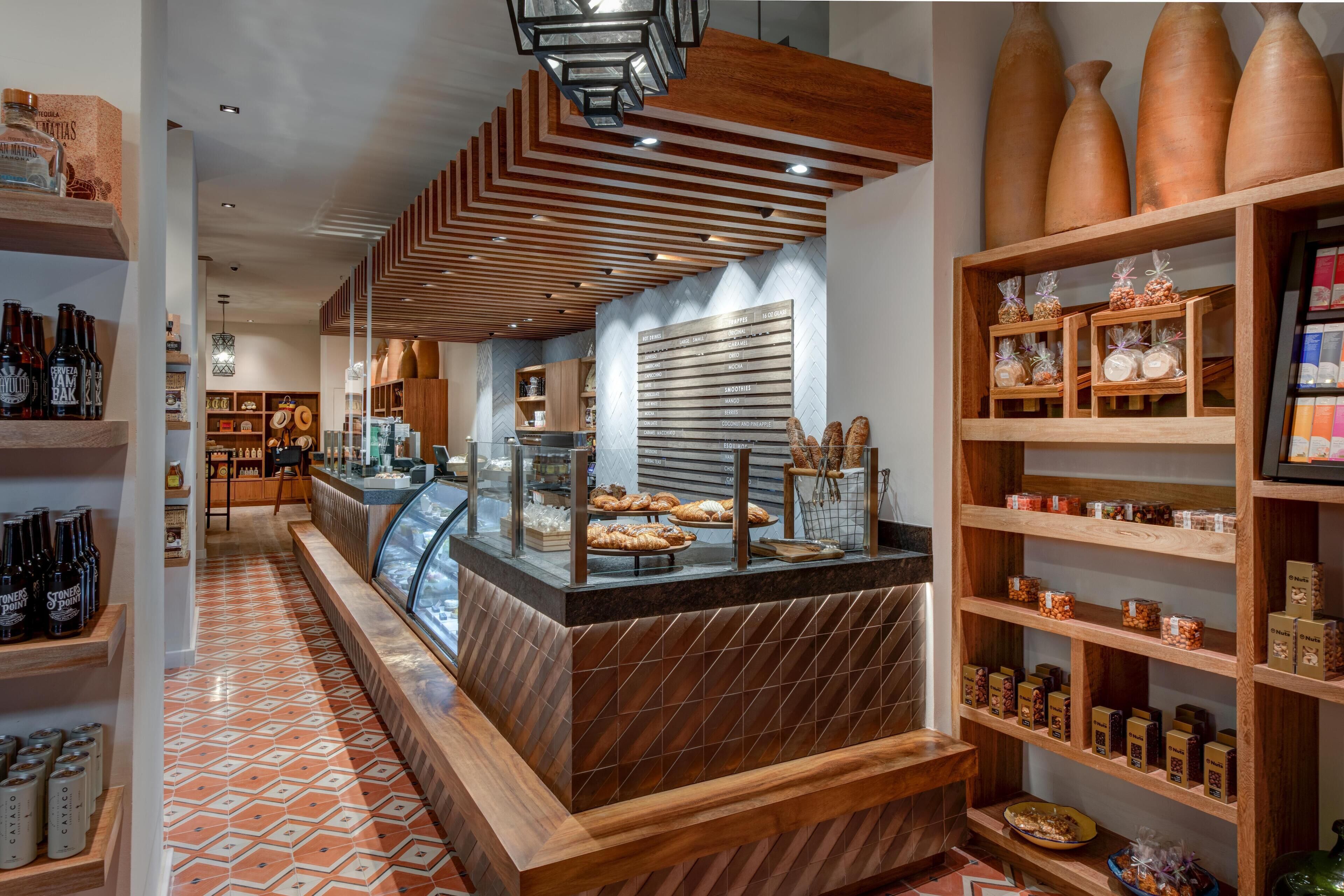 A bakery counter with pastries, a display of bottles, and a wooden shelf with jars.