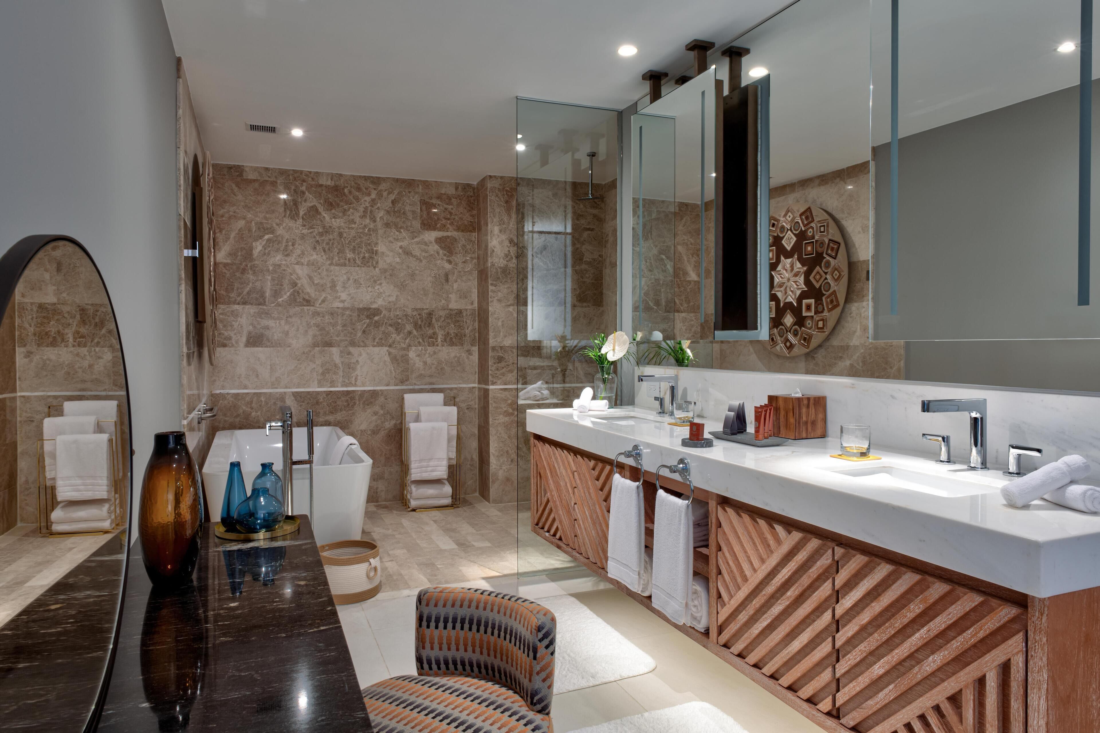 A modern bathroom with a large mirror, a vanity with a wooden cabinet, and a seating area with a chair.