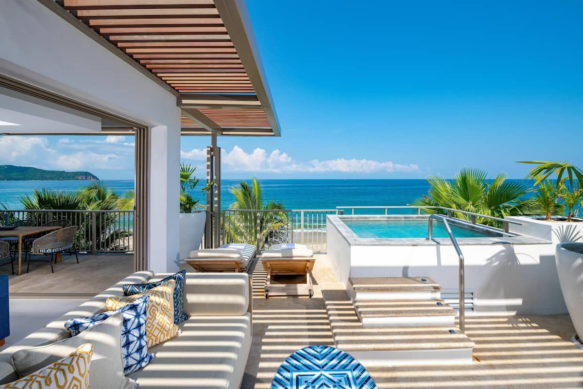 A rooftop pool area with a view of the ocean, outdoor seating, and a covered patio.