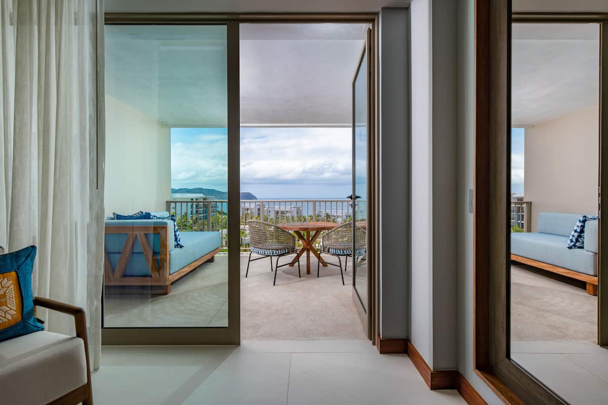 A hotel room with a balcony, a sofa, a dining table, and chairs.