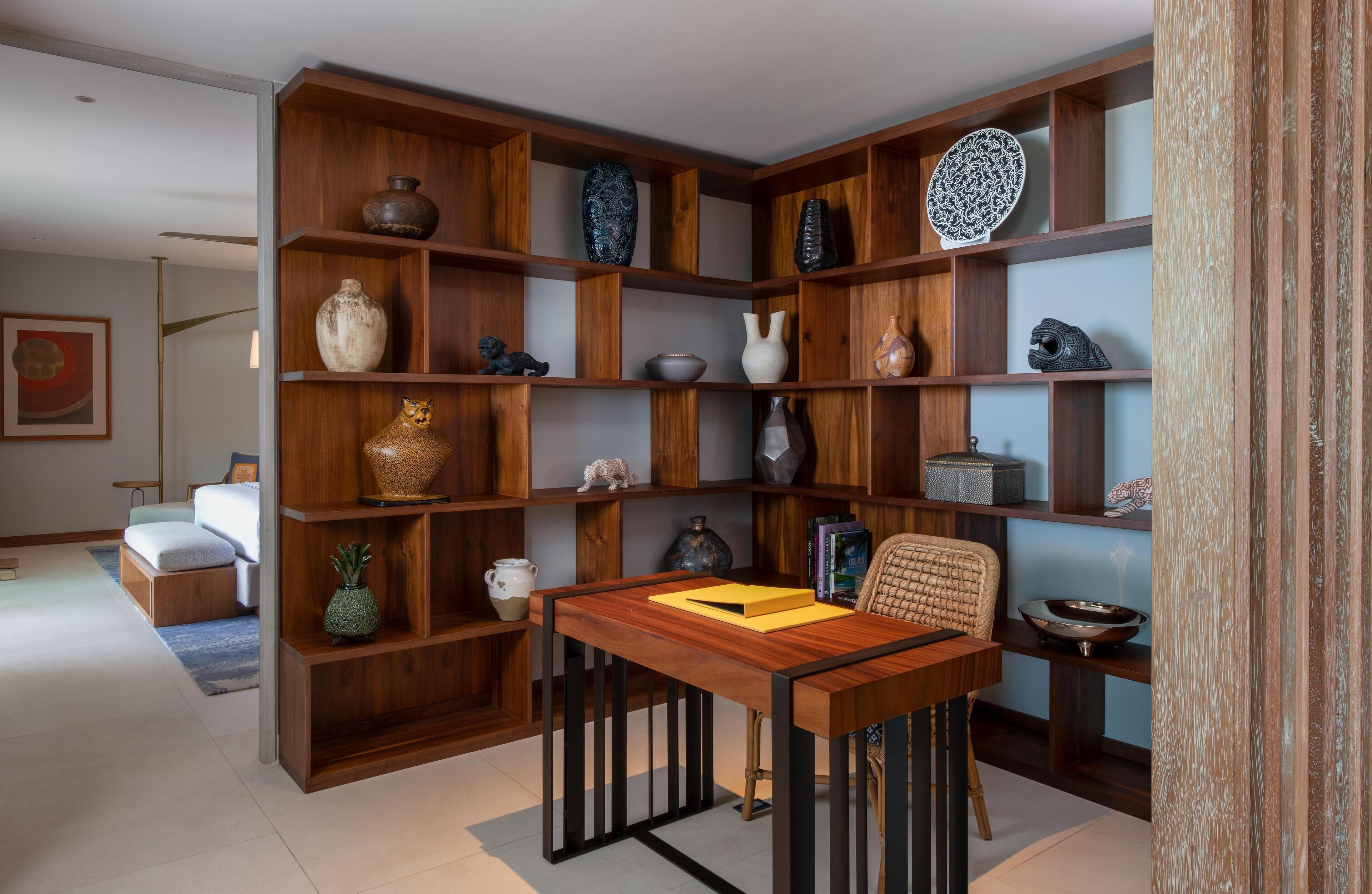 Een moderne woonkamer met een houten boekenkast vol decoratieve objecten, een eettafel met stoelen en een bank.