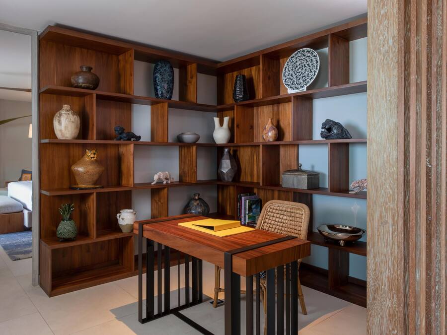 Een moderne woonkamer met een houten boekenkast vol decoratieve objecten, een eettafel met stoelen en een bank.