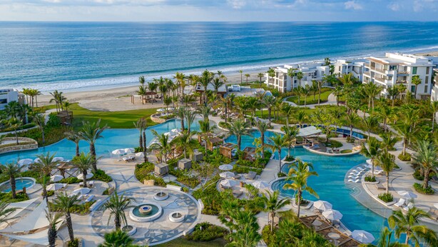 Un resort con una piscina grande, palmeras y vistas al océano.