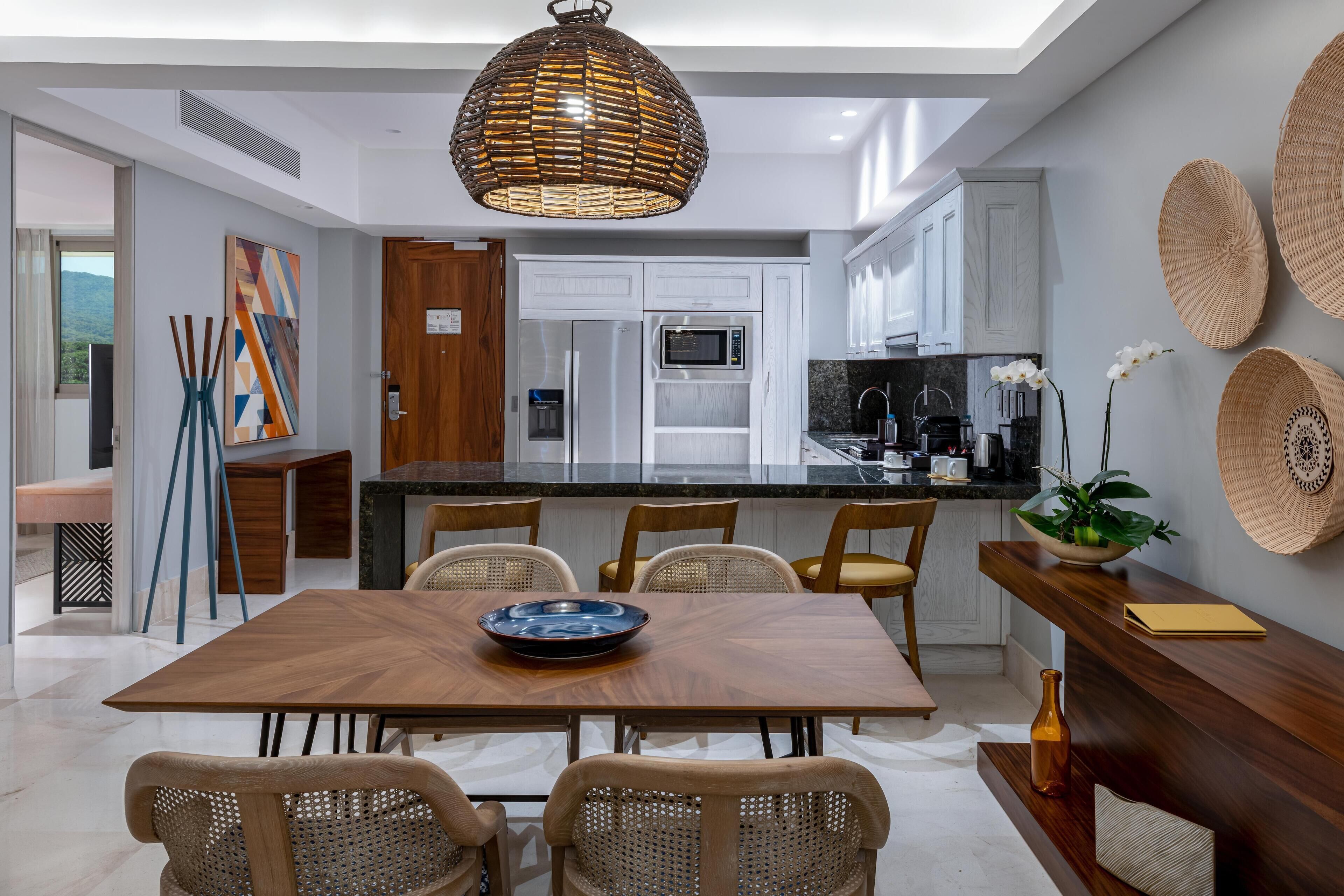 Una cocina moderna con armarios blancos, una isla central y una zona de comedor con mesa de madera y sillas de mimbre.