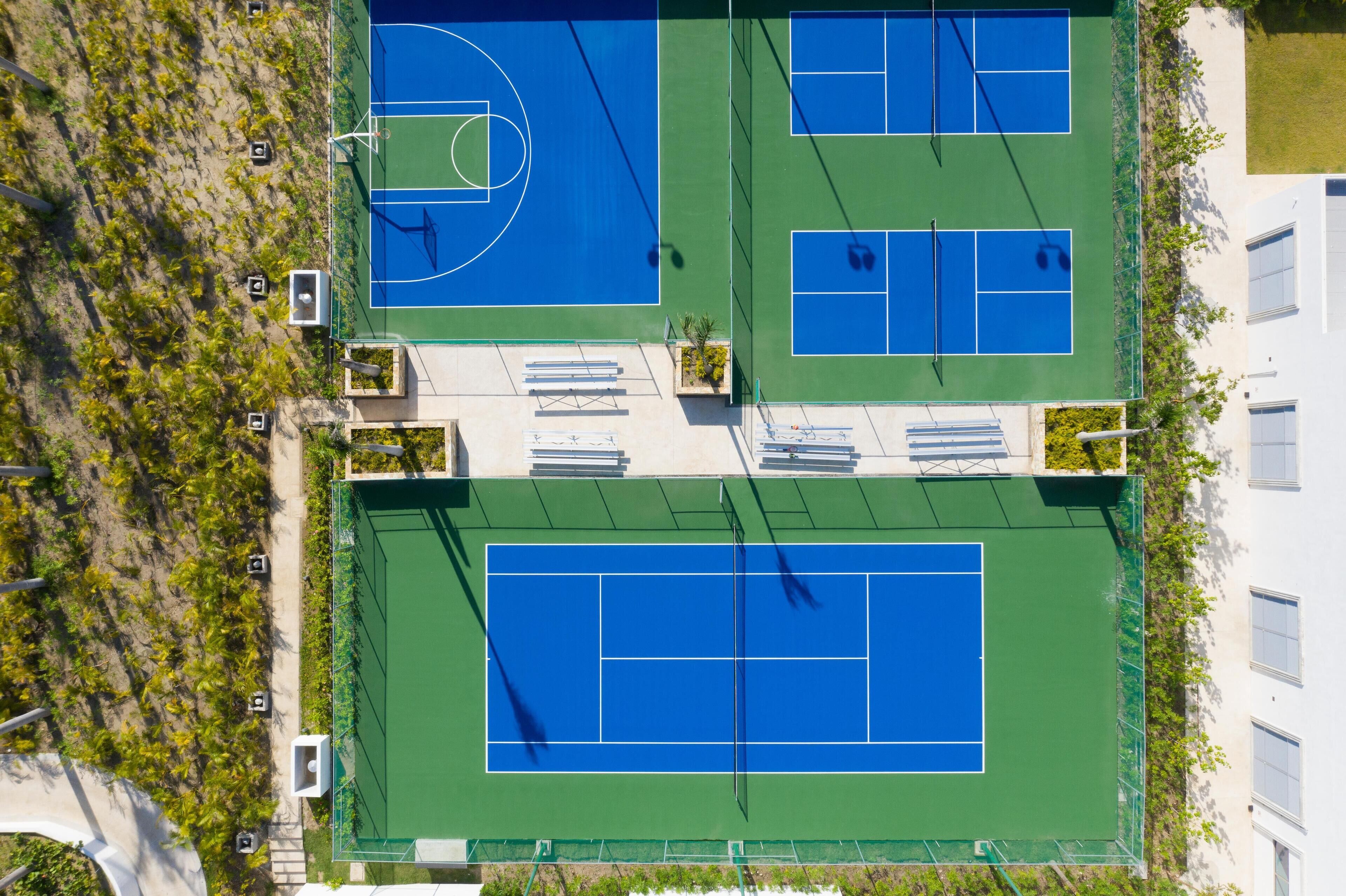 An aerial view of a tennis court complex with multiple courts, seating areas, and a surrounding landscaped area.