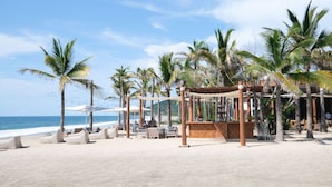 Una playa con palmeras, sillas de descanso y una zona de bar.