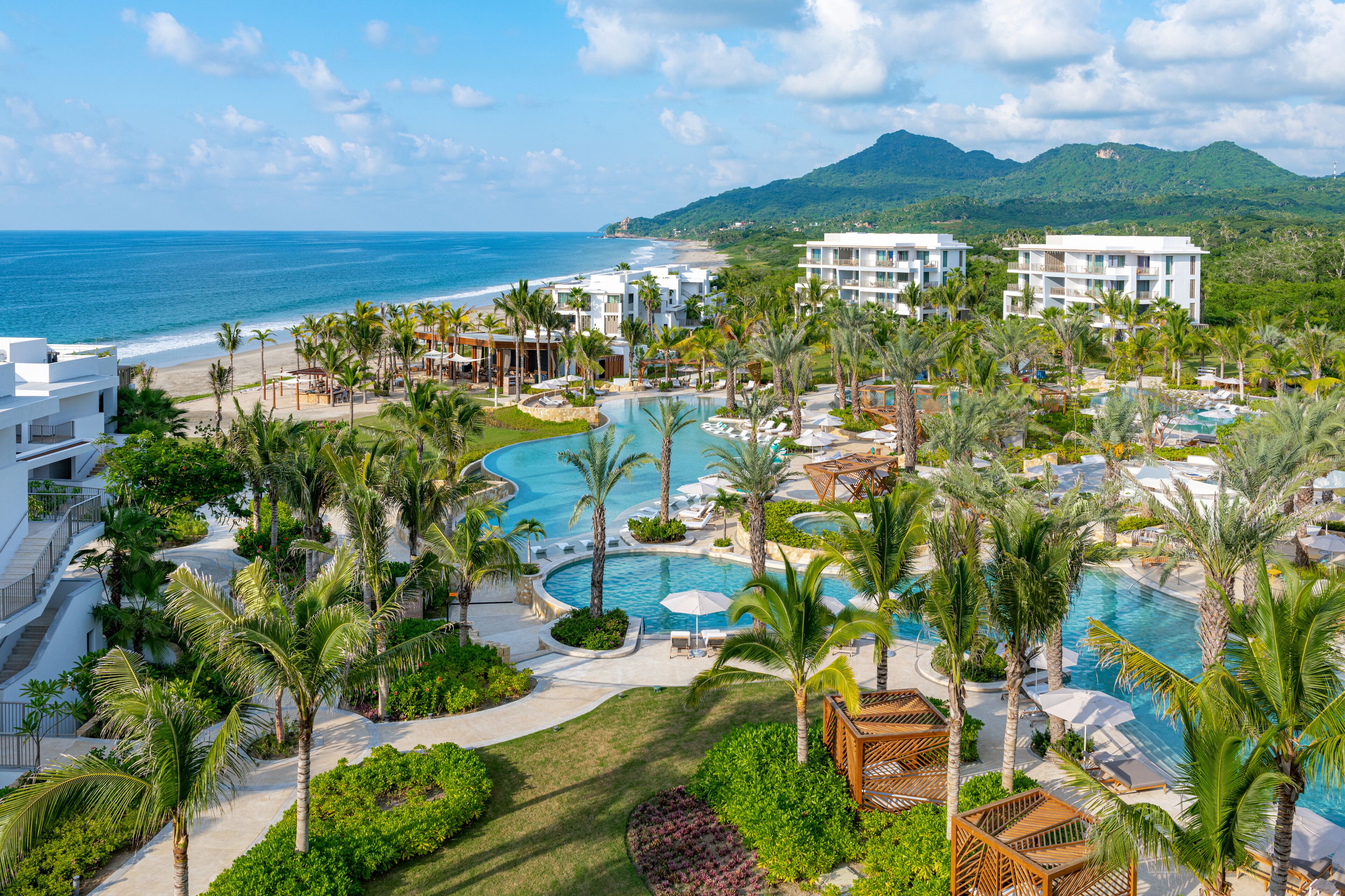 A resort with a large pool, palm trees, and a view of the ocean.