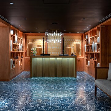 A reception area with a wooden reception desk, shelves with vases and bottles, and a patterned floor.