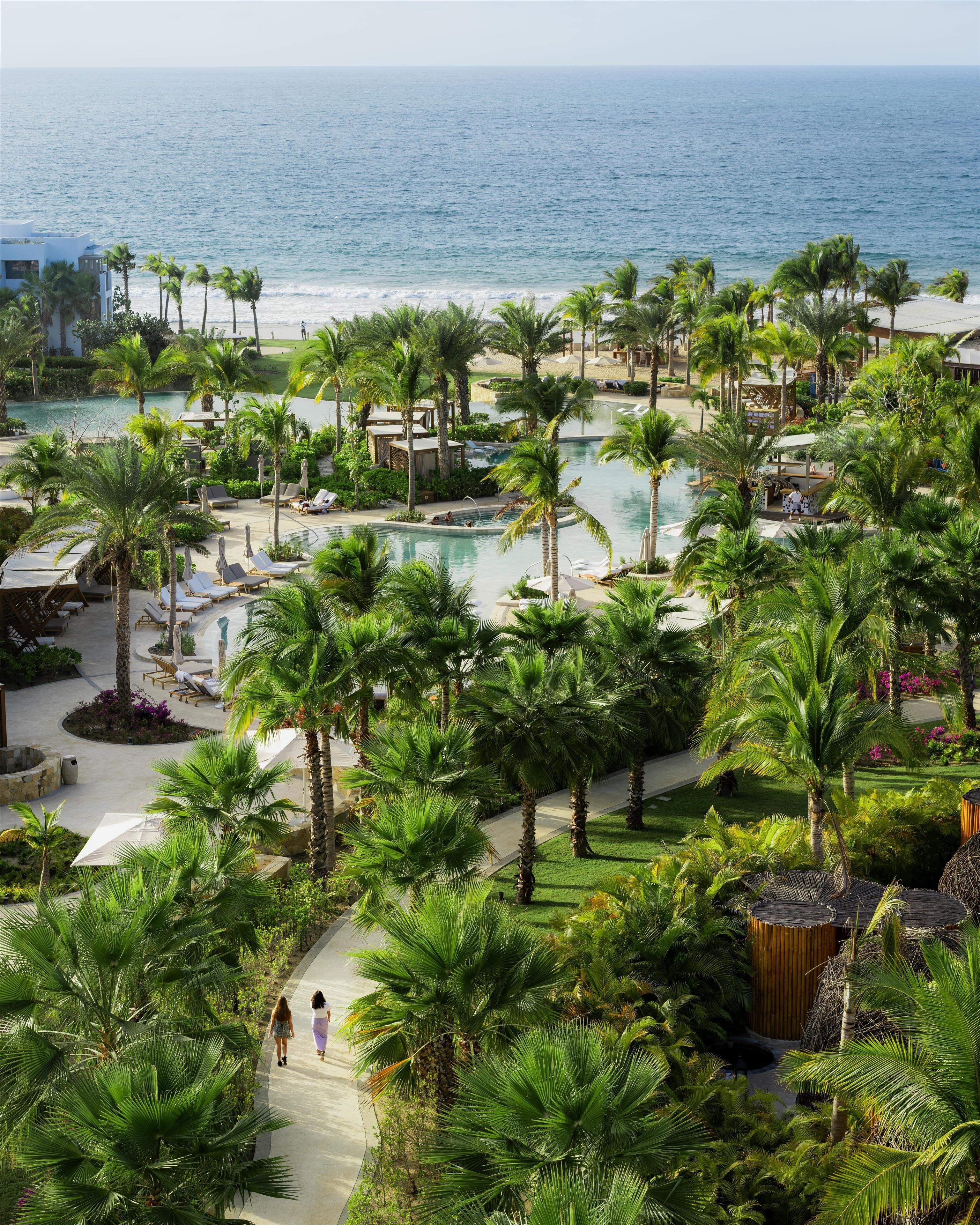 Een resort met een groot zwembad, omringd door palmbomen, een strand en uitzicht op de oceaan.